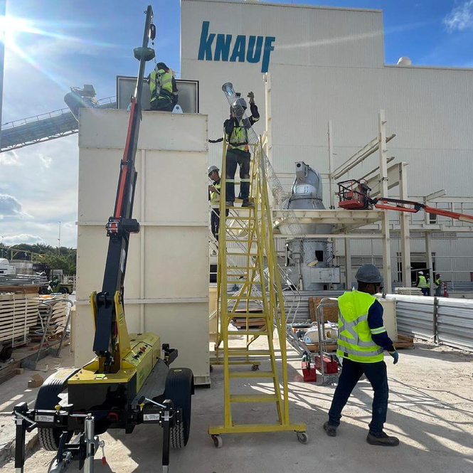Dois trabalhadores usam o AMX simultaneamente em fachada industrial da Knauf, garantindo segurança em altura.